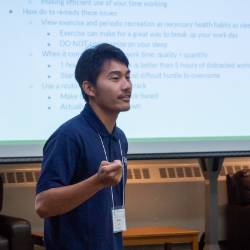 Presenter wearing a lanyard speaks at a past Colloquium