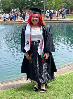 Shannon Lowry in graduation attire standing on a shoreline.
