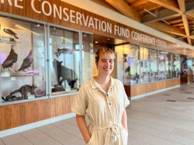 Woman in a white jumper standing in front of a bunch of taxidermied animals behind glass cases. Text at the top says "Conservation Fund Conference Center"