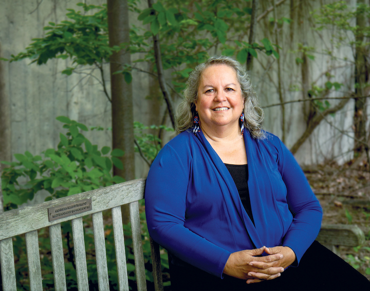 woman in blue sweater sitting on a bench with trees in the background