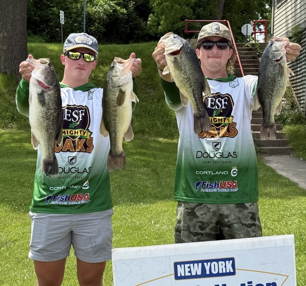 Two young men in white ESF jerseys, wearing baseball hats and sunglasses, holding two bass each