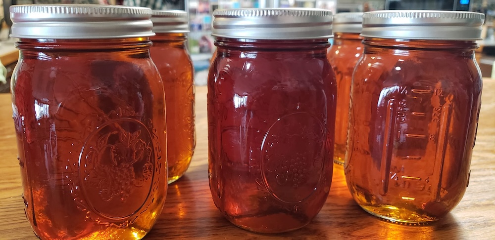 Three jars of maple syrup sitting on a shelf.