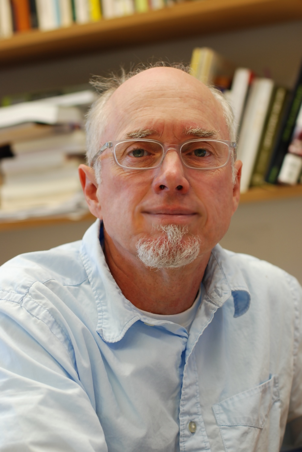 Man with glasses sitting in front of bookcase.