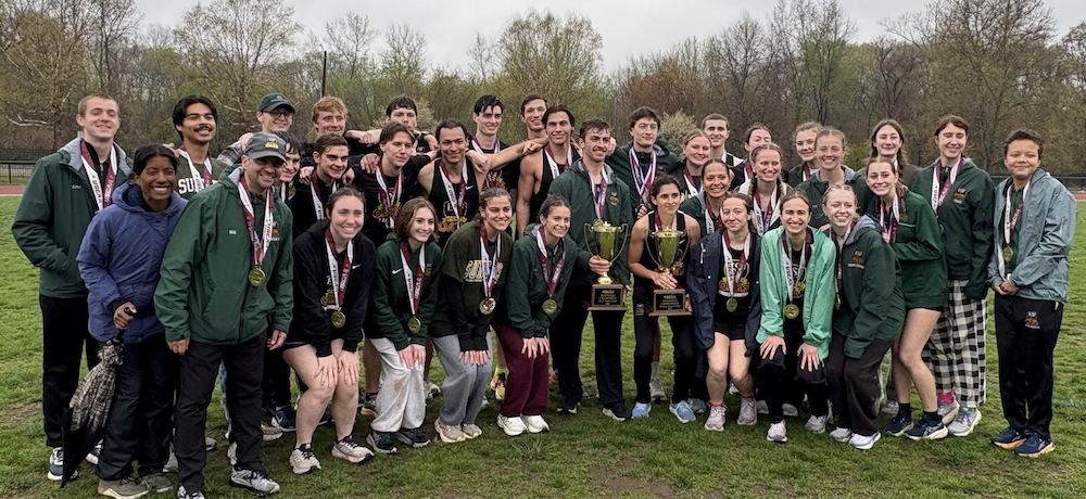 Group of young men and women posing with two large trophies standing outside.