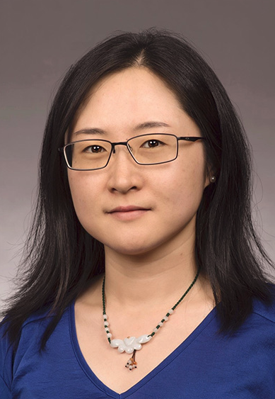 Young woman with shoulder length hair wearing glasses, a blue shirt and a necklace.