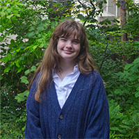 Person in a blue cardigan smiles in front of a background of trees